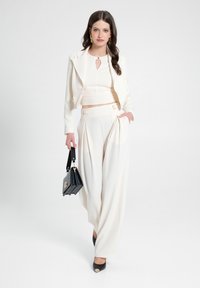 Giacca crema con rever a punta, top crop abbinato e pantaloni larghi. Borsa nera e tacchi a punta con accenti dorati.