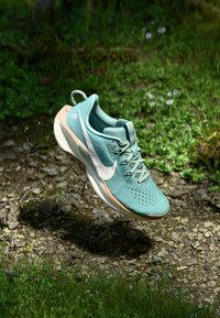 Running shoe in teal mesh with white Nike swoosh, textured surface, pink sole, and lightweight design, set against a natural background.