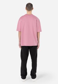 Tricou oversized roz deschis cu mâneci scurte, din material din bumbac, cu decolteu rotund și o croială lejeră, asortat cu pantaloni negri și adidași albi.