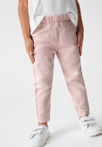 Pantaloni rosa chiaro con fascia elastica in vita, dal taglio tapered, con tasche laterali e dettagli di cucitura sottili, abbinati a sneakers bianche.
