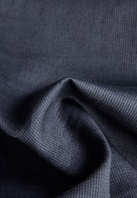 Mörk marinblått tyg med en strukturerad, ribbad mönstring, som har mjuka draperingar och en subtil lyster. Mjukt, lättvikts- och flexibelt material.