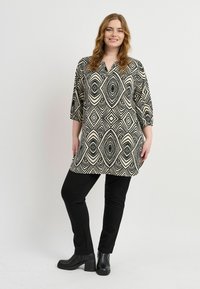 Schwarz-creamfarbener Tunika-Top mit geometrischem Diamantmuster, Dreiviertelärmel, kombiniert mit figurschmeichelnden schwarzen Hosen und Stiefeletten.