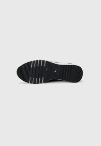Semelle de chaussure en caoutchouc noir avec des rainures horizontales et des accents blancs ; présente une pointe arrondie et une surface texturée pour une meilleure adhérence.