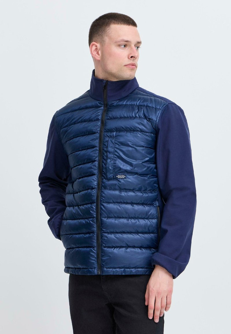 Mornarska puffer jopica z zadrgo spredaj, horizontalnim kvačkanim vzorcem, visokim ovratnikom in kontrastnimi modrimi rokavi. Sprednji žep in slim fit oblikovanje.