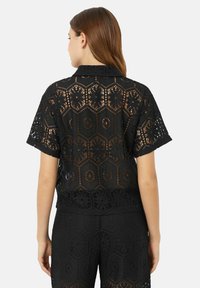 Zwarte t-shirt met korte mouwen, versierd met een ingewikkeld hexagonaal kantpatroon, een kraag en een open ontwerp, gecombineerd met bijpassende onderstukken.