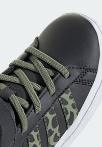 Černé kožené tenisky se zelenými tkaničkami, texturované zelené boční akcenty s kamuflážním vzorem a bílou gumovou podrážkou.