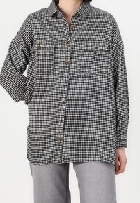 Koszula w stylu houndstooth w czarno-białym kolorze, zapinana na guziki, luźny krój z dwiema przednimi kieszeniami i guzikami w odcieniu drewna. Miękka, fakturowana tkanina.
