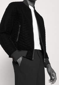 Svart kviltad bomberjacka med dragkedja framtill, ribbade ärmslut och krage, med sidofickor och en slät innerfoder.