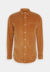 Camisa de pana marrón con botones, cuello, mangas largas y un bolsillo en el pecho. Presenta canalé vertical y botones blancos.