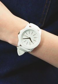 Orologio in silicone bianco con quadrante rotondo, design del quadrante minimalista, indicatori delle ore argentati e cinturino testurizzato, indossato a un polso.