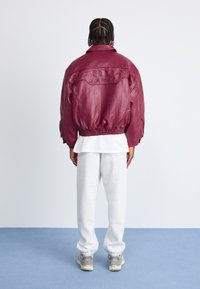 Bordeaux leren jack met een ontspannen pasvorm, elastische tailleband en geëmbosserde tekst "BERLIJN". Gepaard met grijze trainingsbroek en sneakers.