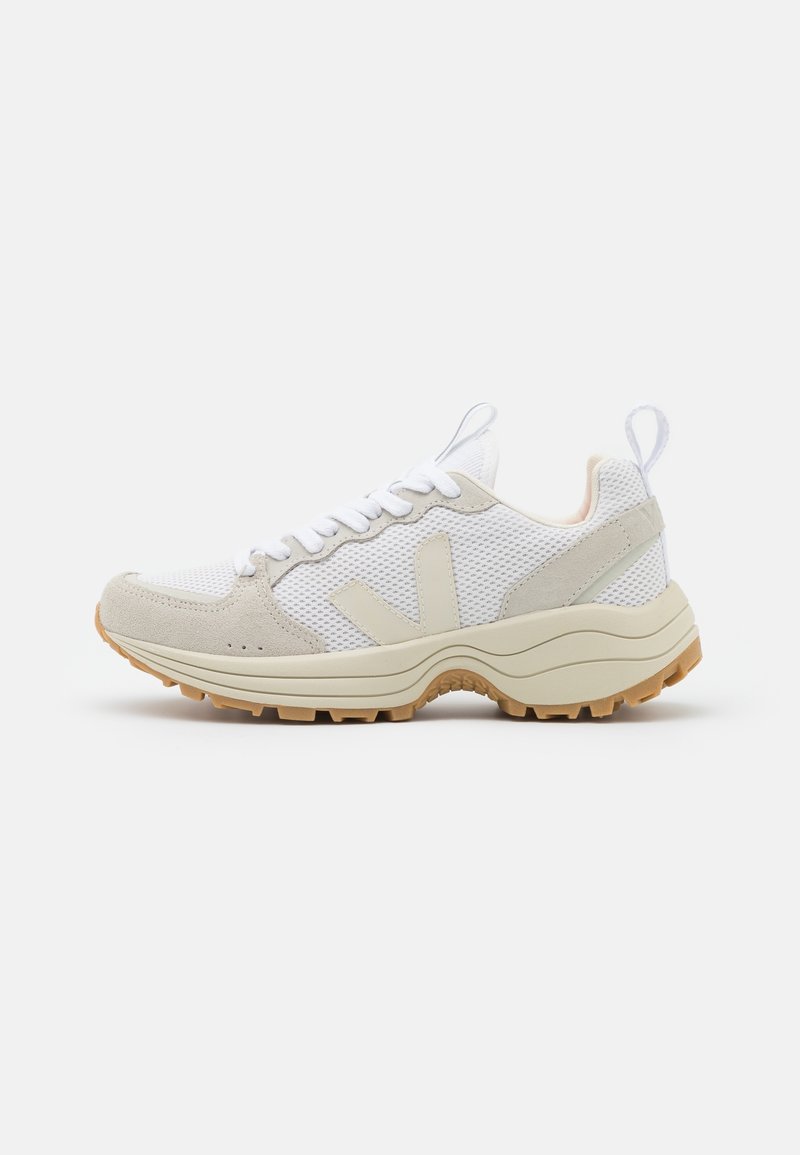 Valkoinen verkkokangas ja beige mokkasneakers, jossa on teksturoitu pohja, paksu, kaareva välikerros ja erottuvat logokoristukset.