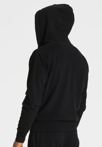 Czarna bluza z kapturem wykonana z miękkiego materiału, z regulowanym kapturem, ściągaczami na rękawach i luźnym krojem. Tył jest gładki, bez grafik.