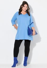 Blaue Tunika mit Dreiviertelärmeln, kombiniert mit schwarzen Leggings und blauen Stiefeletten. Die Tunika hat eine lässige Passform und eine weiche Textur.