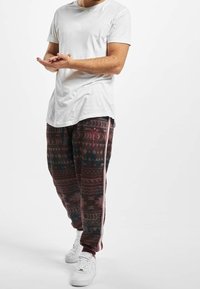 Biała koszulka, ciemnobrązowe spodnie dresowe z wzorem geometrycznym w kolorach różowym i zielonym, oraz białe trampki z teksturowanymi detalami.