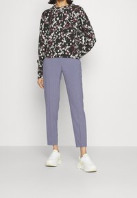 Černý svetr s květinovým potiskem, spárovaný se světle purpurovými kalhotami. Model má na sobě bílé tenisky se žlutými akcenty. Neformální outfit.