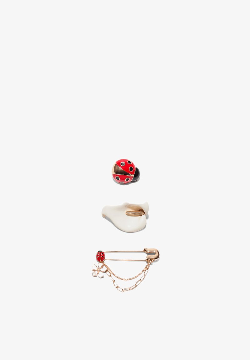 Broche coccinelle rouge et noire, clip blanc en forme de coquillage, et épingle de sûreté dorée avec breloques coccinelle et fleur sur fond blanc.