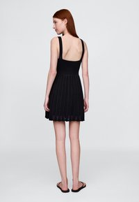 Črna pletena obleka z oprijetim korzetom, odprtim hrbtom in razširjeno krilco z teksturiranim vzorcem. Tanke naramnice in obrobe z valovitim robom.