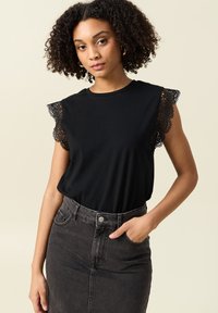 Svart kortärmad topp med spetsdekorerade axelpartier, tillsammans med en högmidjad svart denimkjol. Enkelt, åtsittande design och textur.