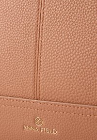 Τσάντα χειρός από υφή δέρματος σε φυσικό ταμπά χρώμα με λεία επιφάνεια, χρυσό λογότυπο της μάρκας και ραμμένες λεπτομέρειες για επιπλέον αισθητική.