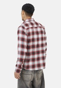 Czerwona i biała koszula flanelowa w kratę z długimi rękawami i kołnierzykiem zapinanym na guziki, charakteryzująca się miękką fakturą i prostym dołem.