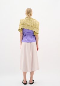 Ljubičasta satenasta bluza, bež lepršava suknja i teksturirani žuti šal draped preko ramena. Crne sandale upotpunjuju cjelokupni look.