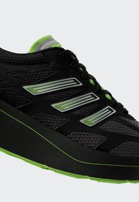 Černá a zelená sportovní teniska s průdušnými panely z mesh materiálu, šněrováním a třemi zelenými pruhovanými reflexními prvky na boku.