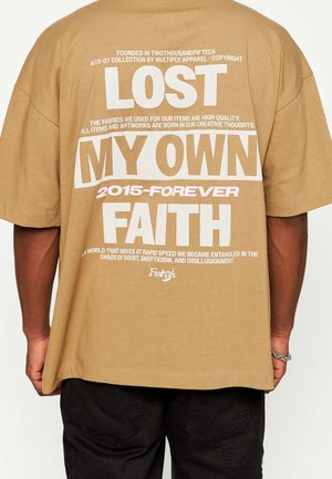 T-shirt oversize en coton marron avec un texte audacieux blanc et rose au dos, comportant un design graphique et une typographie variée. Manches courtes, coupe décontractée.