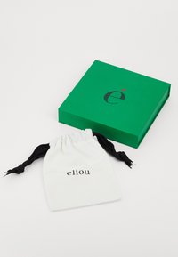 Green box with a black logo and red accent next to a white drawstring bag labeled "eliou" with black cords. Simple, minimalist design.