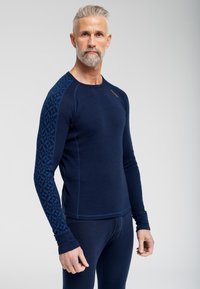 Marine langærmet termisk skjorte med et mønstret blåt stof på den venstre ærme, rund hals og tætsiddende design.