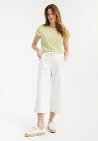 Top verde claro de manga corta con cuello redondo; combinado con pantalones de pierna ancha blancos y zapatillas de plataforma crema.