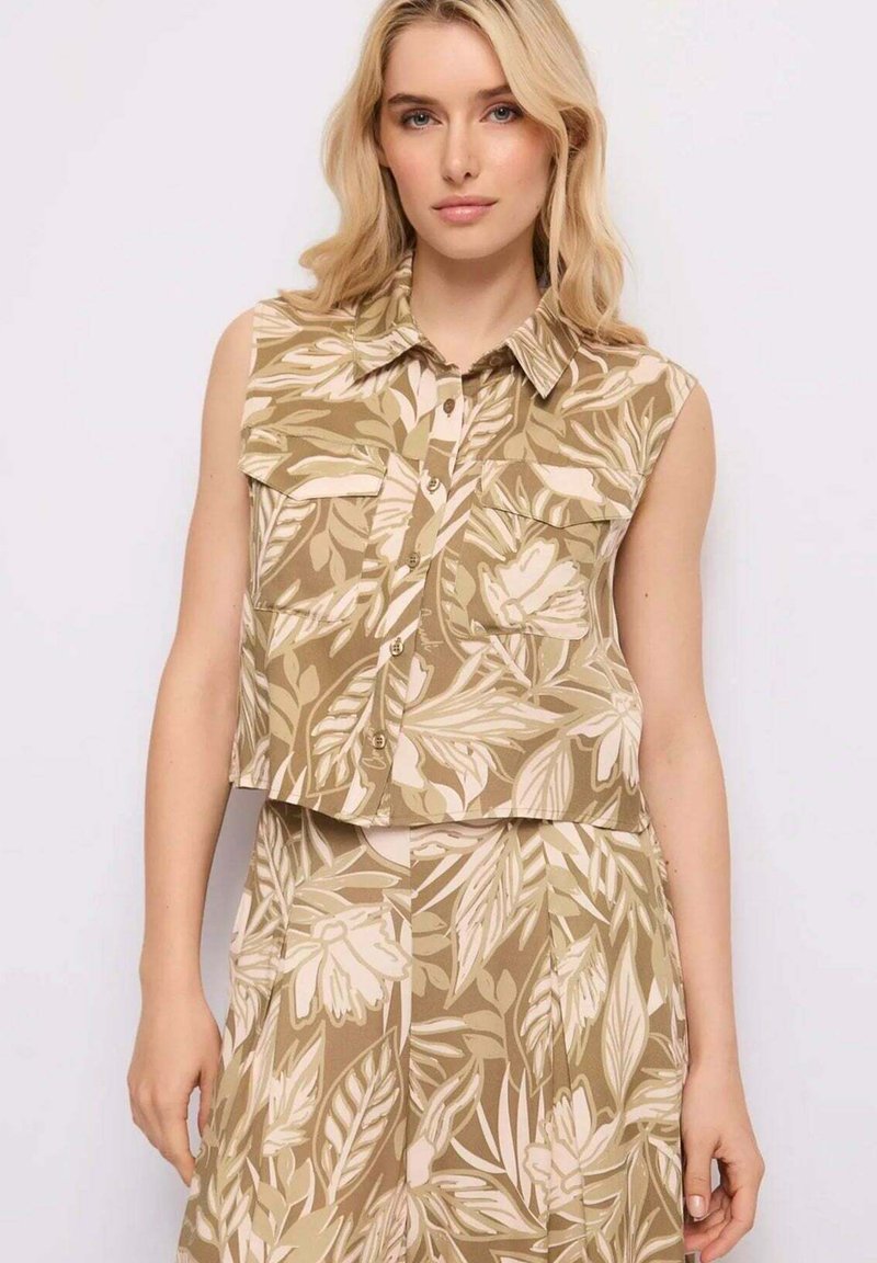 Donna con top senza maniche con colletto e bottoni e gonna abbinata con motivo floreale e foglie beige e bianche.