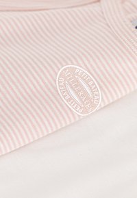 Ριγέ ροζ ύφασμα που επικαλύπτει ολόλευκο ύφασμα. Διαθέτει τονικό κεντημένο λογότυπο με τη λέξη "Petit Bateau" στην ροζ περιοχή.