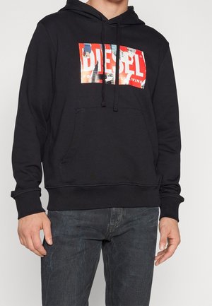 Felpa nera con cappuccio e tasca frontale tipo marsupio. Presenta un'etichetta grafica rossa e blu con il testo "DIESEL" in uno stile usurato. Tessuto morbido, vestibilità standard.