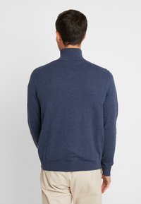 Marinblå tröja med hög krage, ribbade ärmslut och nederkant; tillverkad av ett mjukt, stickat material. Enkla, klassiska design.