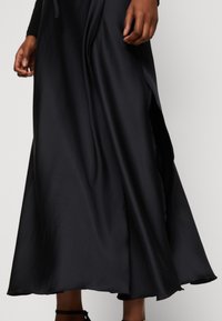 Jupe maxi en satin noir avec une fente latérale, une texture lisse et un design fluide qui s'enroule gracieusement autour des jambes.