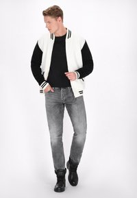 Jachetă bomber albă cu mâneci negre și manșete în dungi, combinată cu un tricou negru și blugi gri. Botine negre completează ținuta.
