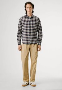 Camicia con bottoni, a trama a quadri blu navy e bordeaux, maniche lunghe e colletto, abbinata a pantaloni beige e sneakers bianche.