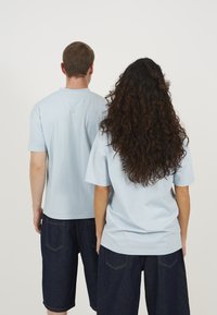 Light blue cotton t-shirts with short sleeves, paired with dark denim shorts. T-shirts feature a relaxed fit and simple design, no patterns.
