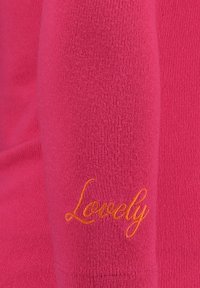 Maglietta a maniche lunghe rosa realizzata in un tessuto a trama. Presenta un ricamo arancione con la scritta "Lovely" sulla manica. Design semplice con forma aderente.