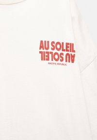 Weißes Baumwoll-T-Shirt mit rotem Drucktext "AU SOLEIL" und "PACIFIC REPUBLIC", mit einem lässigen Rundhalsausschnitt und kurzen Ärmeln.