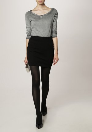 Maglia grigia a maniche lunghe con scollo tondo e dettaglio di bottoni, abbinata a una mini gonna nera texturizzata, collant neri e décolleté con borchie.