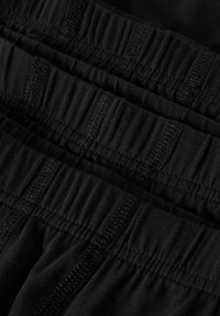 Cztery ułożone na stosie czarne bokserki męskie z elastycznymi pasami i widocznymi detalami przeszyć, widok z bliska.