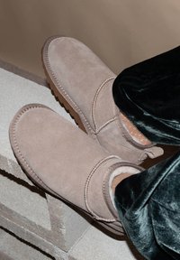 Helle beigefarbene Wildleder-Stiefeletten mit runder Zehenpartie, weicher Innenausstattung und strukturiertem Gummisohle, mit gesticktem Rand und Rückenschlaufen-Detail.