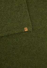 Oliwkowy, dziany szal wykonany z miękkiego materiału, z nieregularnym brzegiem i małą brązową metką z logo. Gładka tekstura.