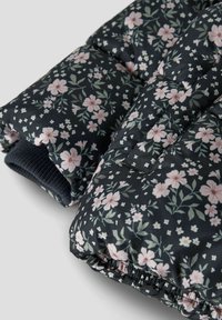 Nahaufnahme des ärmels einer schwarzen gepolsterten Jacke mit einem rosa und weißen Blumenmuster sowie einem gerippten Strickbund.