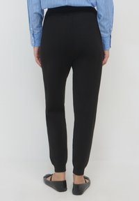 Schwarze Strickhose mit elastischem Bund, schmal zulaufendem Schnitt und gerippten Bündchen. Der Look wird mit einem blau-weiß gestreiften Hemd kombiniert.