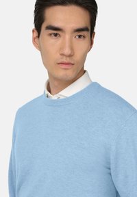 Hemdblauwe trui van zacht materiaal, met een ronde hals en lange mouwen. De textuur lijkt glad en licht gebreid.