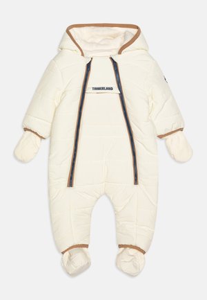 Combinaison de neige rembourrée couleur crème pour bébé avec capuche, moufles, chaussons, double fermeture éclair avant et logo Timberland sur le rabat de poitrine.