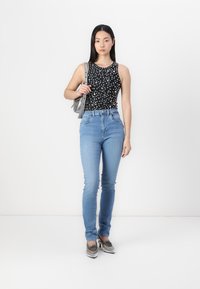 Top negro sin mangas con lunares blancos, jeans ajustados azul claro y zapatos trenzados plateados brillantes, sosteniendo un bolso metálico.